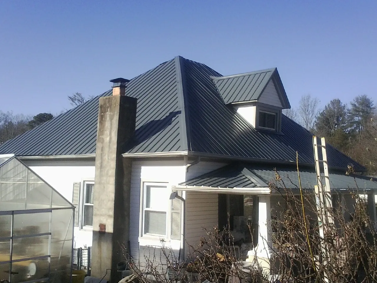 Dark blue standing seam metal roof on a white farmhouse with dormer — Slate & Tile Roof Repair by Roofing Brothers in Kenyon