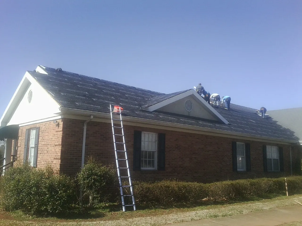 Crew tearing shingles off a brick ranch roof with a ladder set — Emergency Roof Repair work by our crew in Kenyon