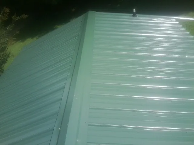 New green metal panels meeting at the ridge of a roof — Flat Roof Repair work by our crew in Kenyon